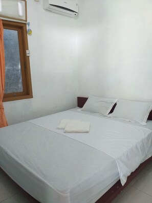 A simple, clean room with a bed, white bedding, a window with curtains, and a wall-mounted air conditioner. - Kenangan Guest House (Sabang)
