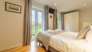A bedroom with a bed, a TV mounted on the wall, and a sliding glass door leading to a balcony. - This spacious, detached holiday home is just a short walk from the beach. (12 Brecon Close)