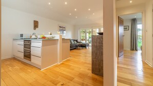 A modern kitchen with white cabinetry, a central island, and a dining area with a gray sofa. - This spacious, detached holiday home is just a short walk from the beach. (12 Brecon Close)
