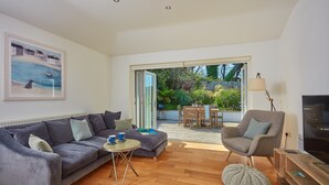 A modern living room with a grey sofa, a round coffee table, and a grey armchair. There is a TV on a wooden stand and a painting on the wall. - This spacious, detached holiday home is just a short walk from the beach. (12 Brecon Close)