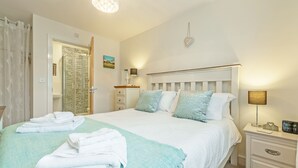 A neatly made bed with white and blue bedding, a bedside table with a lamp, and a wall-mounted heart decoration. - This property is an ideal, and very green choice for your family holiday. (32, Ashton Close)