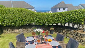 A table set outdoors with wicker chairs, a striped tablecloth, and a bottle of champagne. - This property is an ideal, and very green choice for your family holiday. (32, Ashton Close)