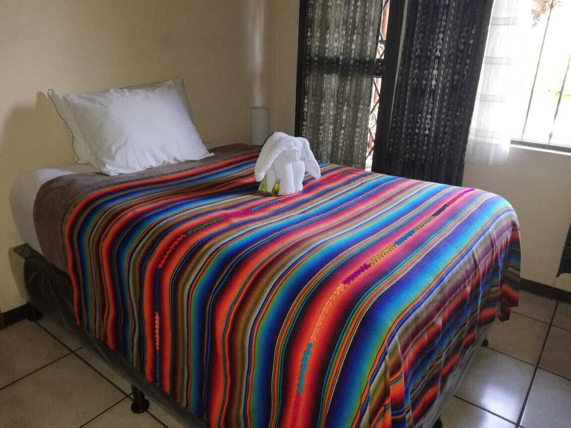 Una cama con una colcha a rayas de colores, una almohada blanca y una toalla blanca a un lado.