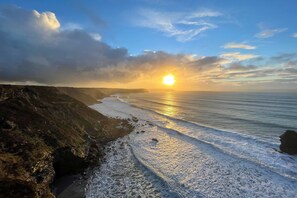 A coastal landscape with a sunset over the ocean, rocky cliffs, and a sandy beach. - With uninterrupted sea views, this property enjoys a superb hillside position. (Lighthouse Hill)