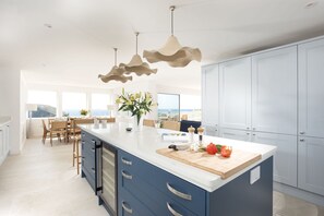 A modern kitchen with a large island, blue cabinetry, and a view to the outdoors.