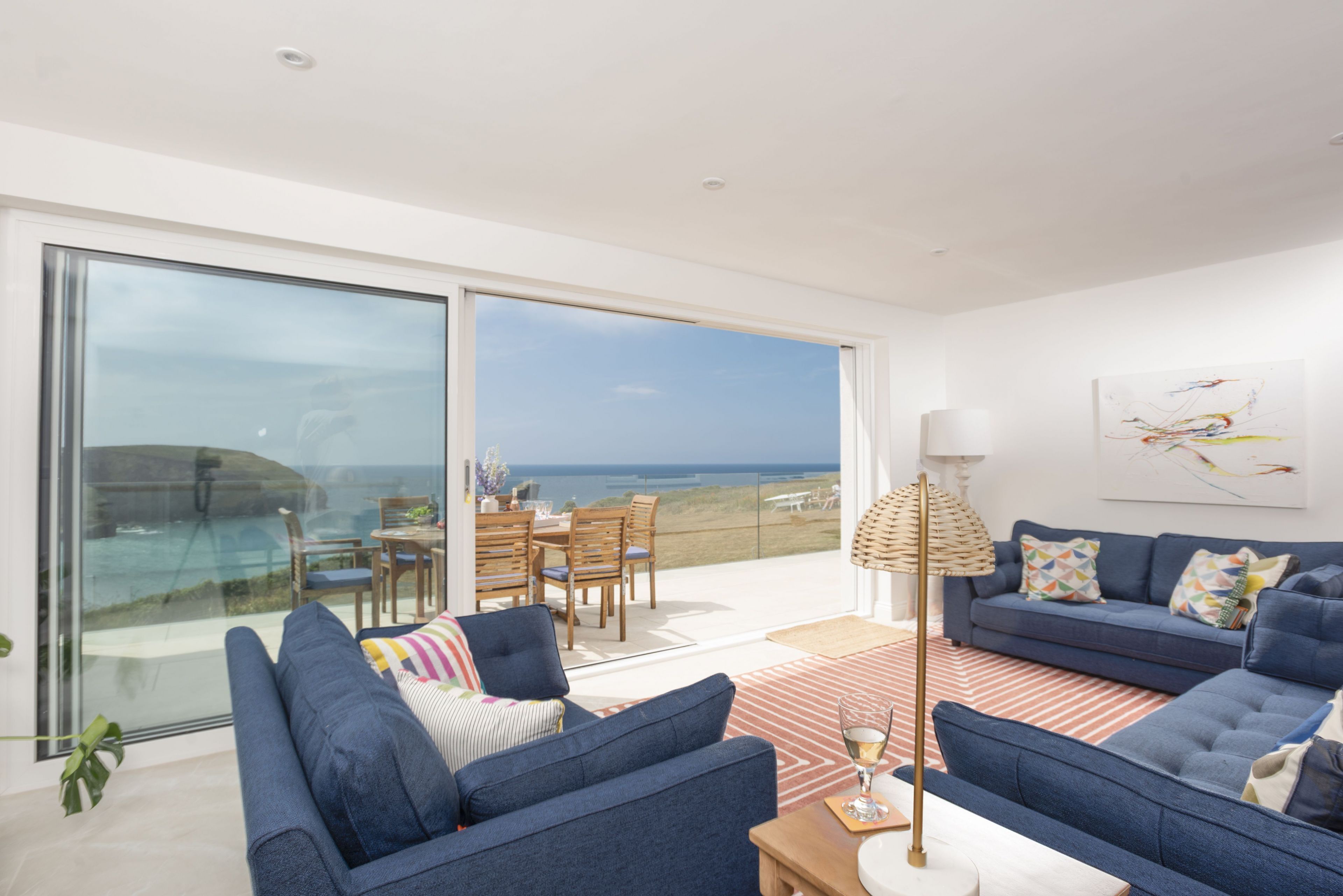 A modern living room with a large sliding glass door leading to a balcony with a view of the sea.