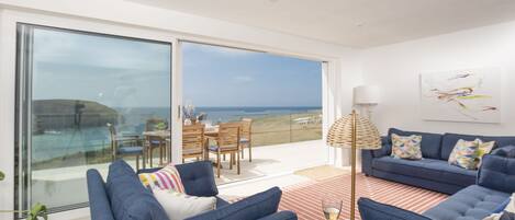 A modern living room with a large sliding glass door leading to a balcony with a view of the sea.