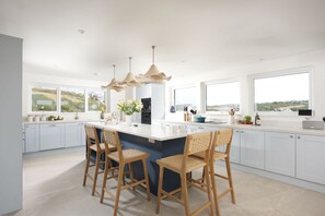 A modern kitchen with a central island, bar stools, and large windows offering a view of the outdoors.