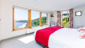 Quarto com uma cama grande, duas janelas com vista para o mar, uma cadeira e um radiador.
