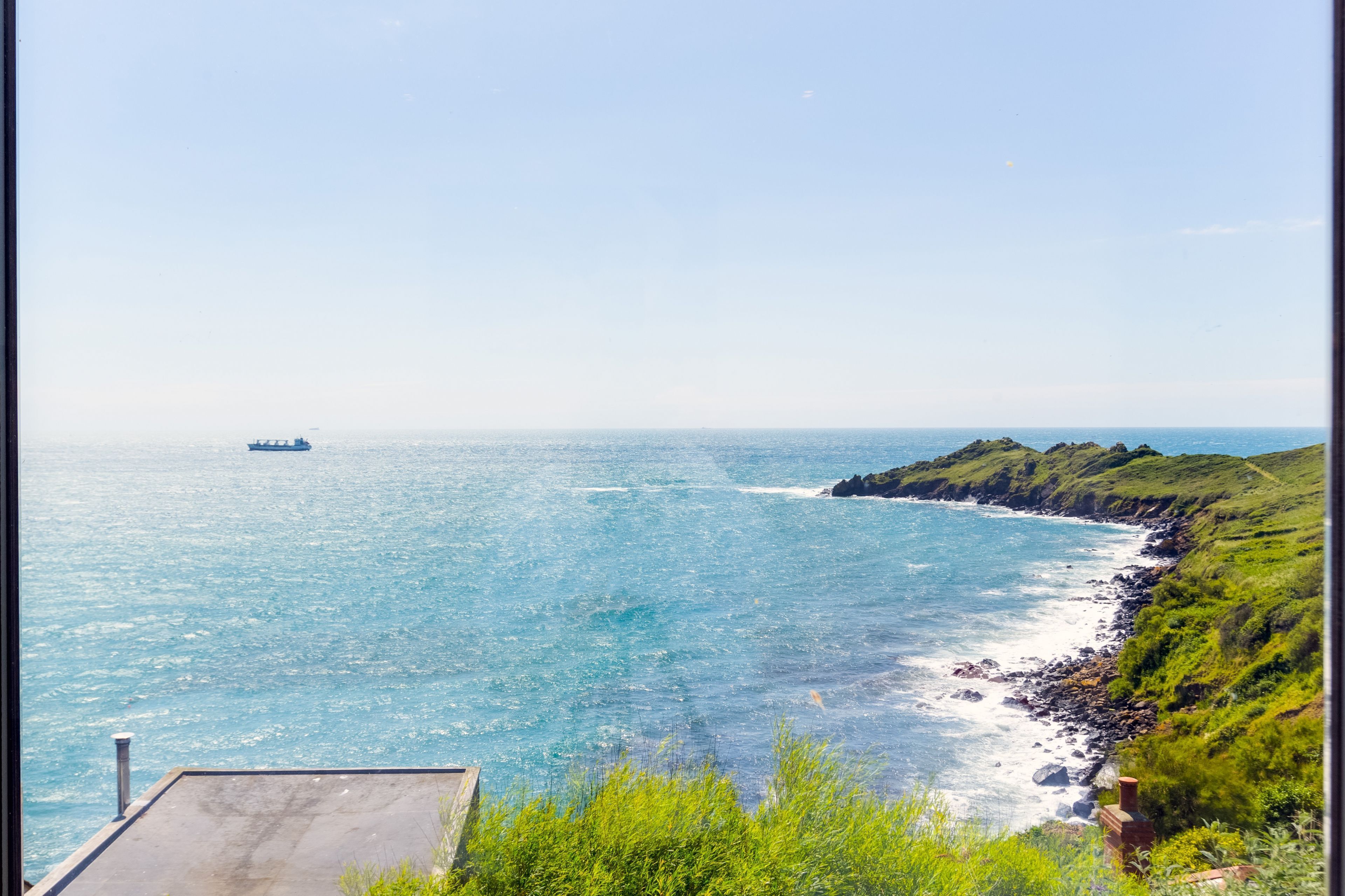 Une vue côtière avec un navire à l’horizon, une côte rocheuse et une végétation luxuriante.
