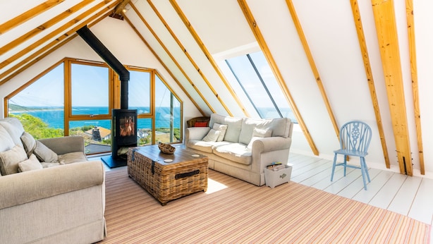 Um quarto de sótão acolhedor, com uma janela grande, lareira e vista para o mar.