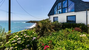 Uma casa costeira com um amplo parapeito, rodeada por vegetação exuberante e vista para o oceano.
