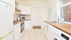 A compact kitchen with white cabinets, a microwave, a washing machine, and a wooden countertop. - Townhouse @ Earle Street Crewe (Crewe)
