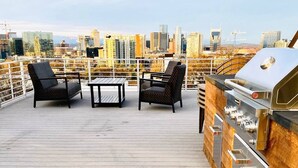 Terraza en la azotea con una parrilla y zona de estar, con vistas a un paisaje urbano.