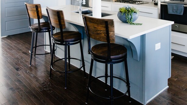 Una cocina moderna con una isla central, taburetes de bar, una lámpara colgante y una puerta corredera.