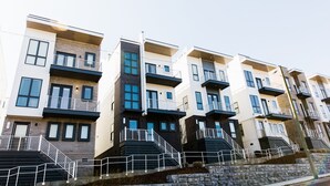 Una hilera de modernos edificios residenciales de varios pisos con balcones, escaleras y un muro de contención de piedra.