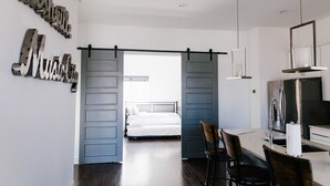 Un dormitorio moderno con cama, escritorio con sillas y una zona de cocina con refrigerador.