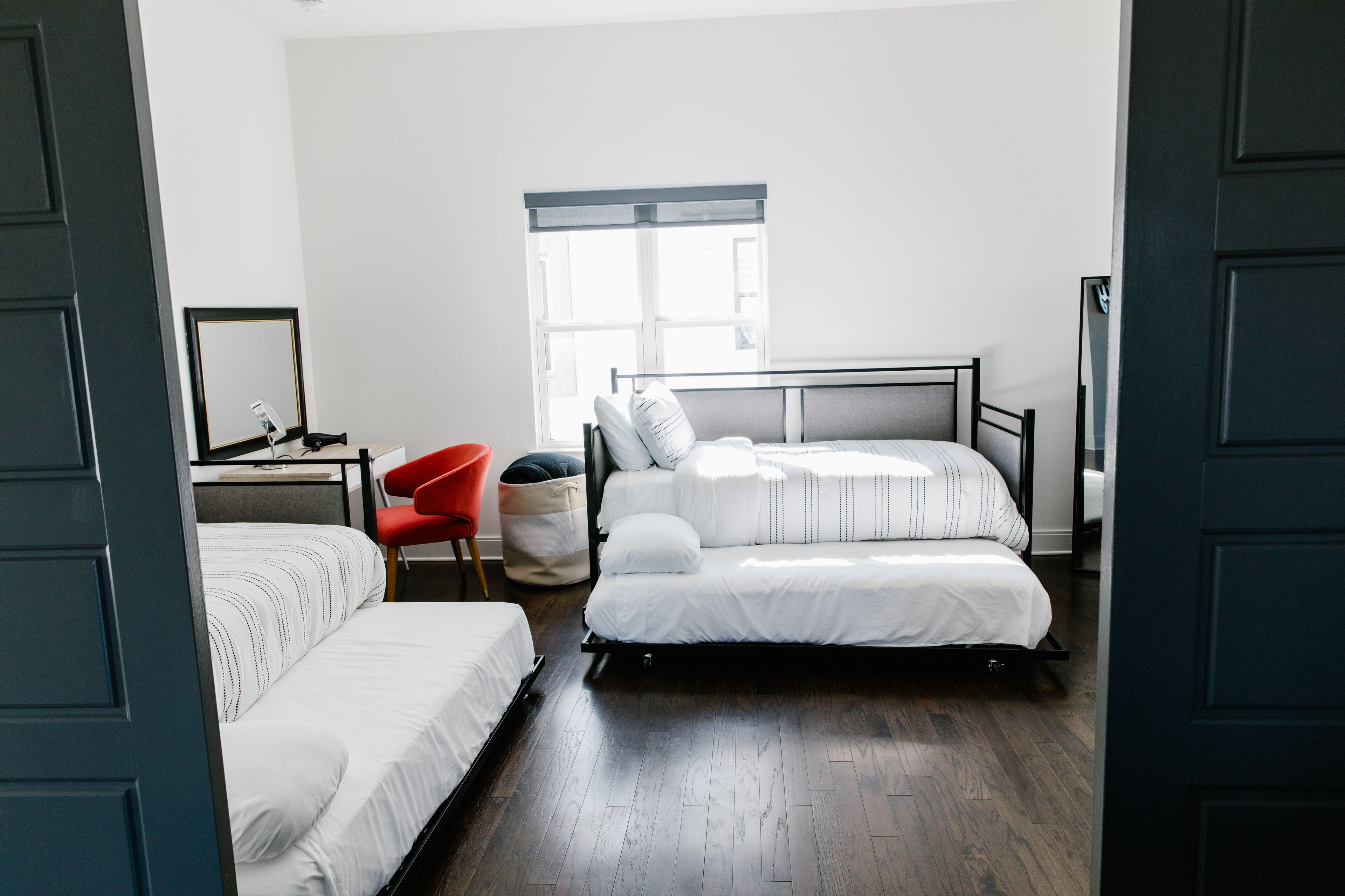 A bedroom with two single beds, a red chair, a desk with a chair, and a window.