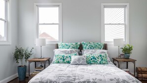 A bedroom with a bed, two bedside tables, a lamp, a potted plant, and a window with blinds. - Bright Charming Guesthouse Close to Downtown DC (Washington)