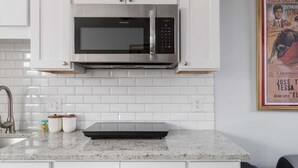 A kitchen with white cabinets, a stainless steel microwave, a marble countertop, a sink, and a framed picture on the wall. - Bright Charming Guesthouse Close to Downtown DC (Washington)