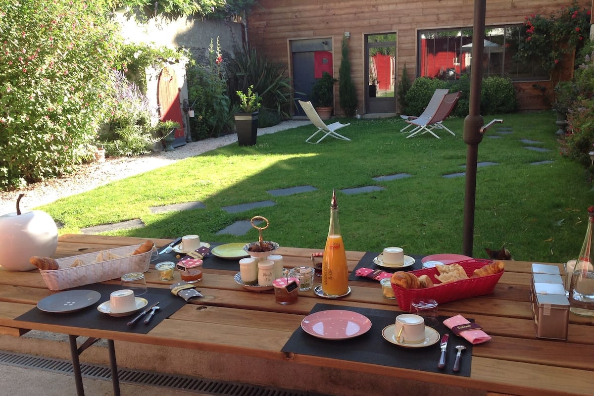Montaje de picnic con una mesa dispuesta para dos personas, con platos, vasos y una botella de jugo de naranja.