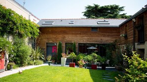A modern wooden house with a well-maintained garden, a patio with outdoor furniture, and a large windowed entrance. - Madeleine & Cie (Angers)