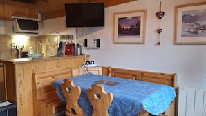A cozy kitchen with wooden cabinets, a microwave, and a sink. There is a dining table with a blue tablecloth and wooden chairs.
