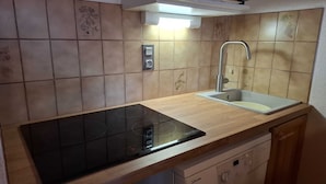 A kitchen with a black induction cooktop, a stainless steel sink, and wooden cabinets.