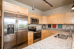 A modern kitchen with stainless steel appliances, granite countertops, wooden cabinets, and a granite backsplash. - ★Glacier Courtyards Condo ★ Walk Everywhere! (Columbia Falls)