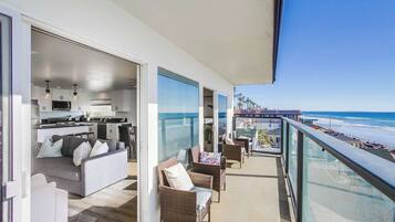 Un balcon avec vue sur la plage, un espace de vie comprenant un canapé et des fauteuils, et une cuisine.