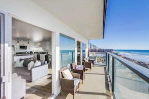 Un balcón con vistas a la playa, una sala de estar con sofá y sillones, y una zona de cocina.