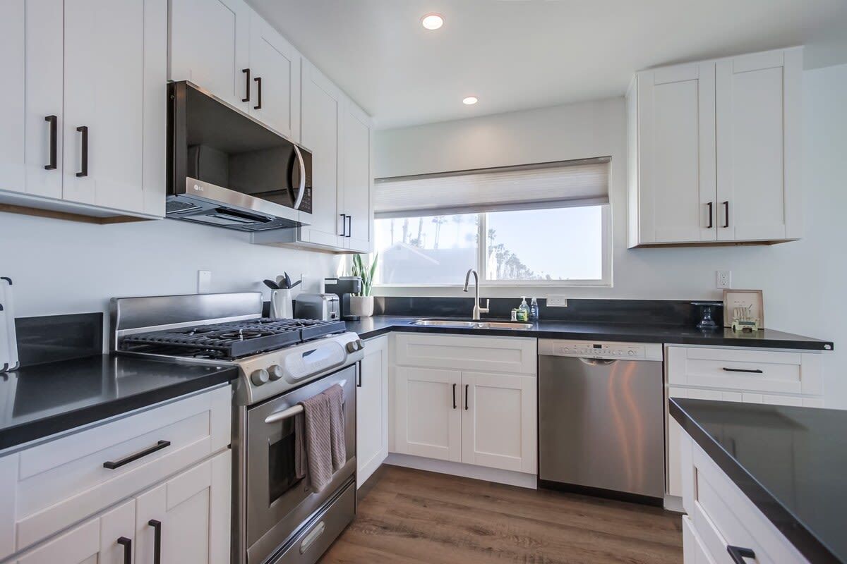 A modern kitchen with white cabinetry, stainless steel appliances, and a black countertop.