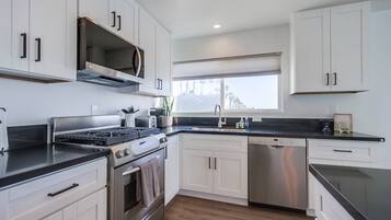A modern kitchen with white cabinetry, stainless steel appliances, and a black countertop.
