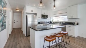 A modern kitchen with white cabinets, stainless steel appliances, and a large island with stools. - The Pier House | A Luxury Oceanfront Penthouse (Oceanside)