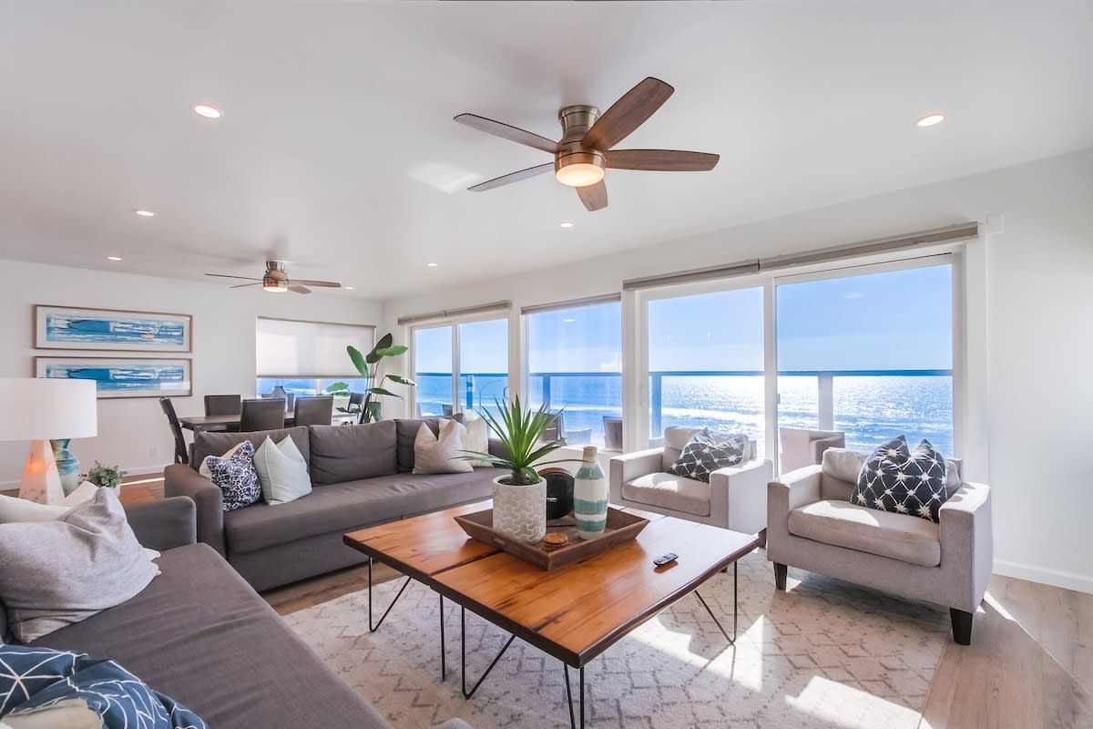 A spacious living room with a large window, a ceiling fan, and a coffee table with decorative items.