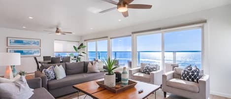 A spacious living room with a large window, a ceiling fan, and a coffee table with decorative items.