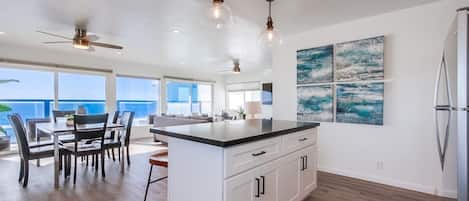 Una cocina amplia con una isla grande, muebles de color blanco e iluminación colgante.