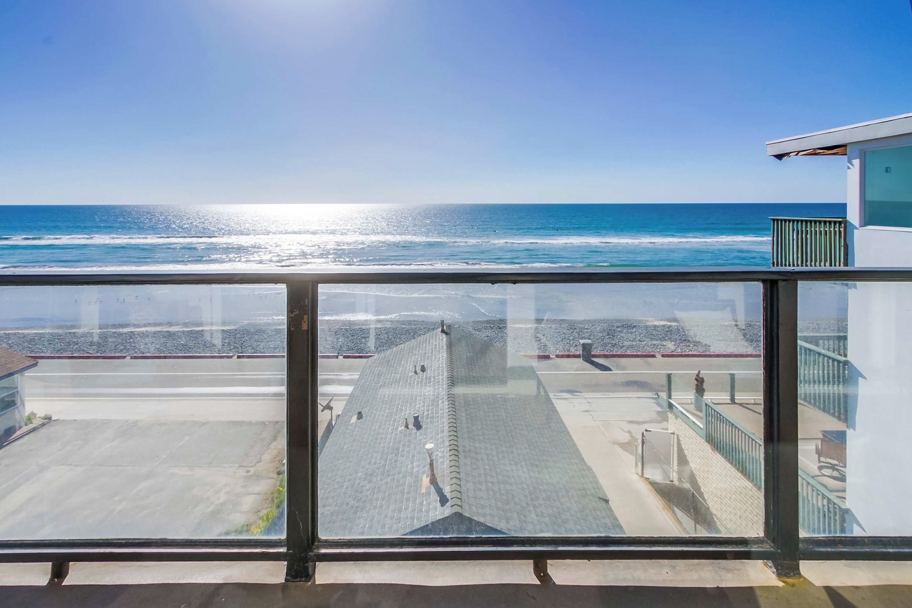 Blick vom Balkon auf einen Strand mit dem Ozean und einem klaren Himmel.