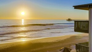 A beach view with a pier in the distance, a balcony with a railing, and a clear sky. - The Pier House | A Luxury Oceanfront Penthouse (Oceanside)
