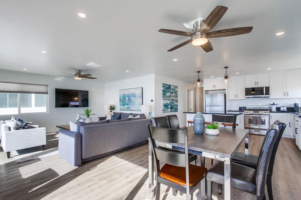 A modern kitchen with white cabinets, a dining area with a wooden table, and a ceiling fan.
