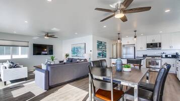 A modern kitchen with white cabinets, a dining area with a wooden table, and a ceiling fan.