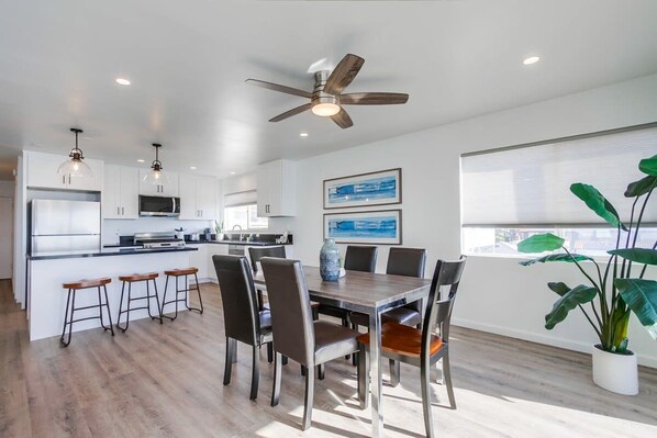 Una cocina moderna con armarios blancos, una isla central y taburetes. Hay una zona de comedor con una mesa y sillas de madera.