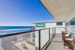 A balcony with a view of the ocean, wicker furniture, and a glass railing.