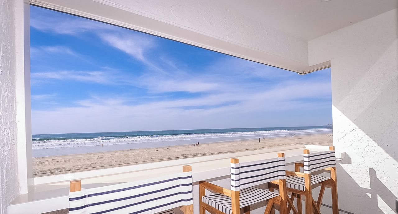 Un balcón con vistas a la playa, con sillas a rayas y una mesa.