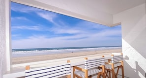 A balcony with a view of the beach, featuring striped chairs and a table.