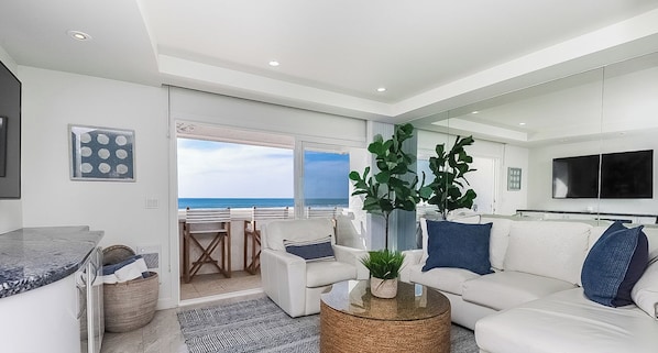 A modern living room with a white sofa, a round coffee table, and a large window overlooking the ocean.