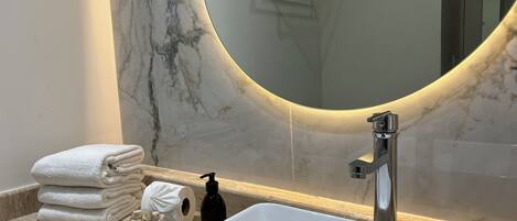 Een badkamer met een wit wastafelmeubel, een marmeren wand en een grote spiegel met een gebogen lijst.