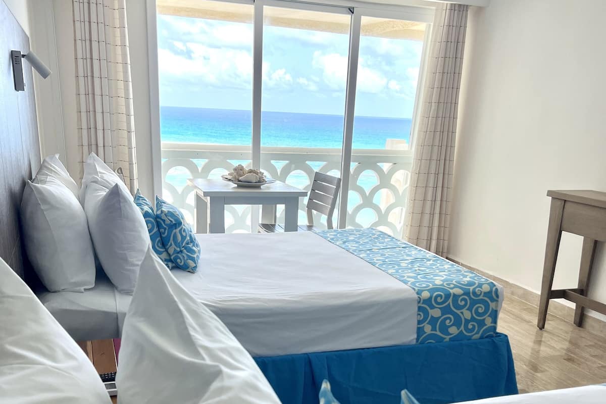 A hotel room with a balcony, a bed with white and blue patterned bedding, and a view of the ocean.