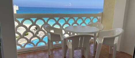 A balcony with a view of the ocean, a white table, and four white chairs.
