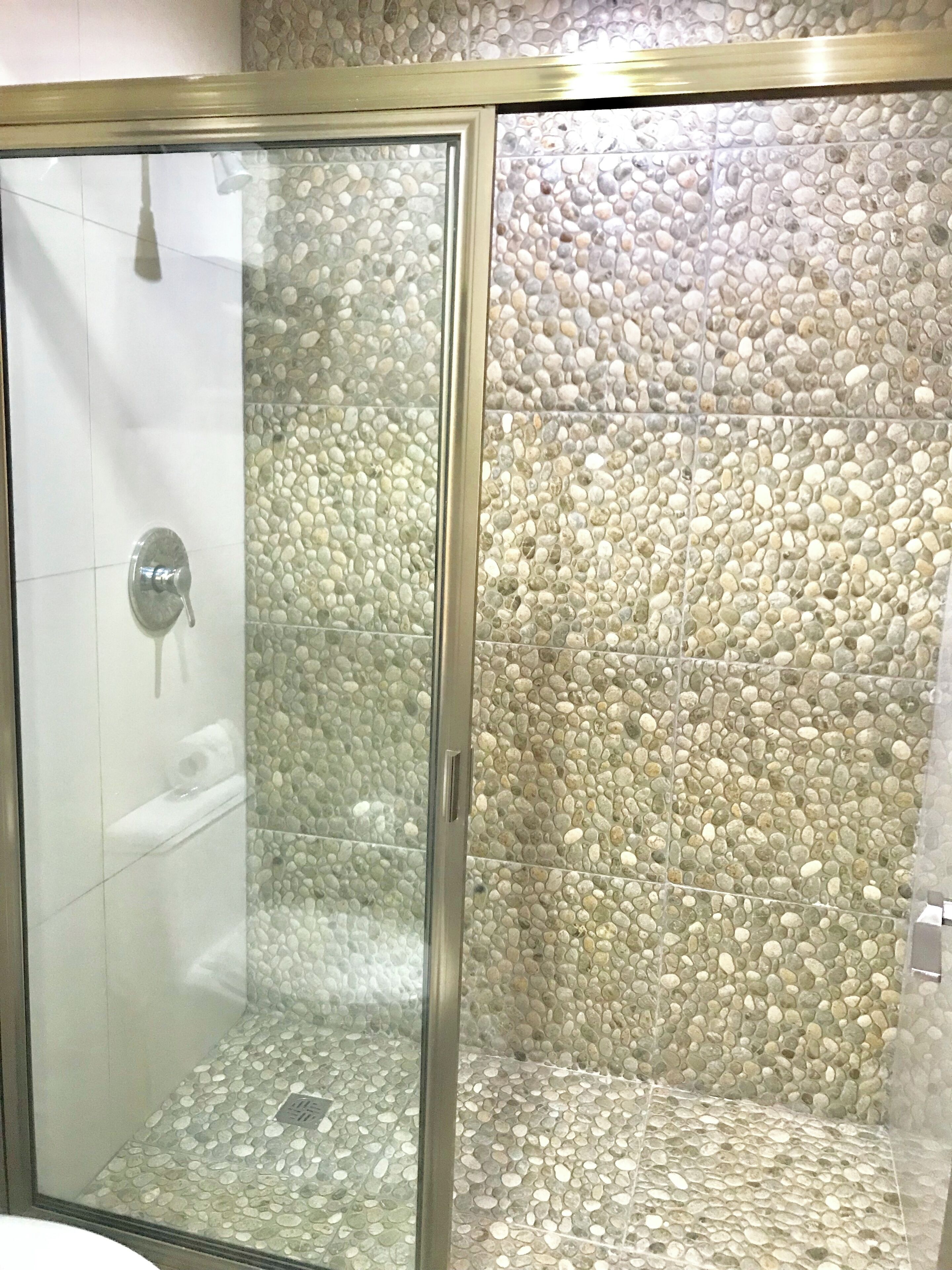 A shower with a glass door and a pebble-textured wall.